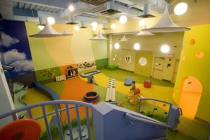 Multicolored shock absorbing carpet at an indoor play room with children playing on play equipment.