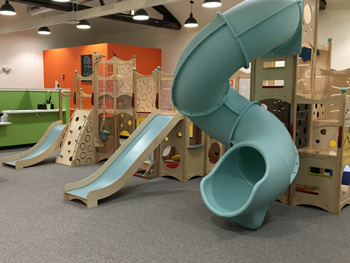Play structure with fall rated carpeting. The carpet is gray in color, and there are three blue slides on the play equipment.