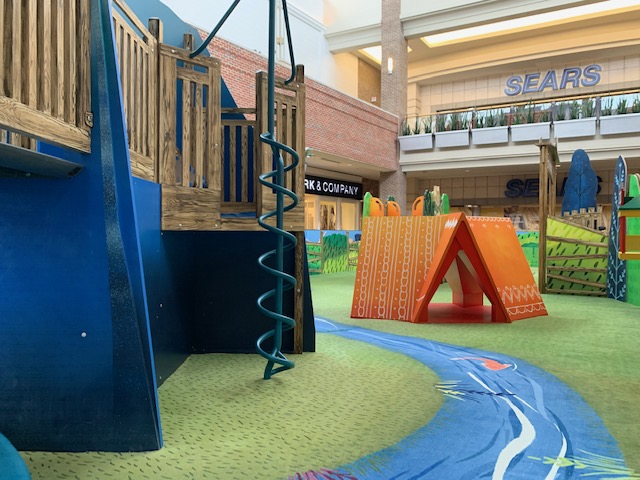 Mall Play area with custom print safe carpet with river design with fish. There are several play fixtures including an orange tent.