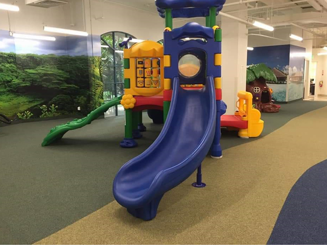 impact absorbing play ground flooring with a custom print, plastic play fixture and trees in the background.
