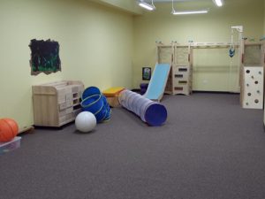 Safe flooring for kids at a community center playroom. There is a small wooden playground, and several tunnels for children to play in.