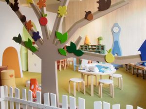Safe Flooring for Kids Daycare play area with white fence, tree, and multiple small tables for kids to play at.