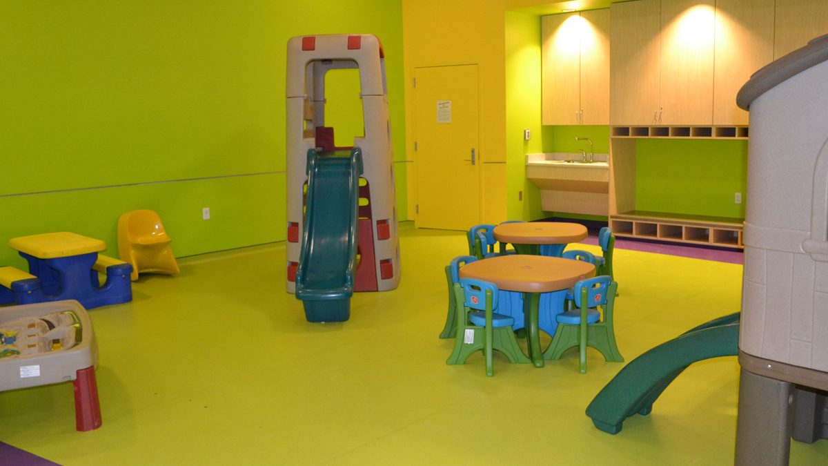 Bright green and purple SafeLandings Resilient Sheet Vinyl System at an indoor day care with small tables and several plastic play equipment.