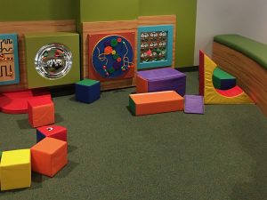 Image of day care flooring with shock absorbing carpeting, puzzel toys on walls and large foam block toys.