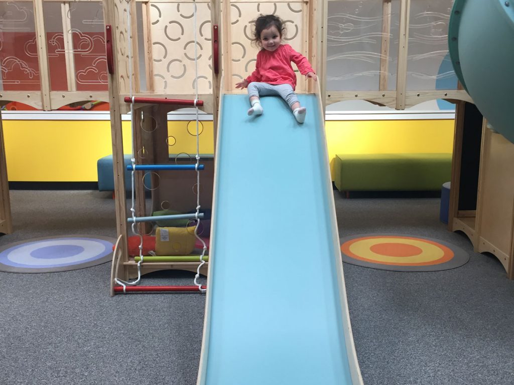 Child sliding down community play things play indoor playground with SafeLandings Shock Absorbing Carpet System.