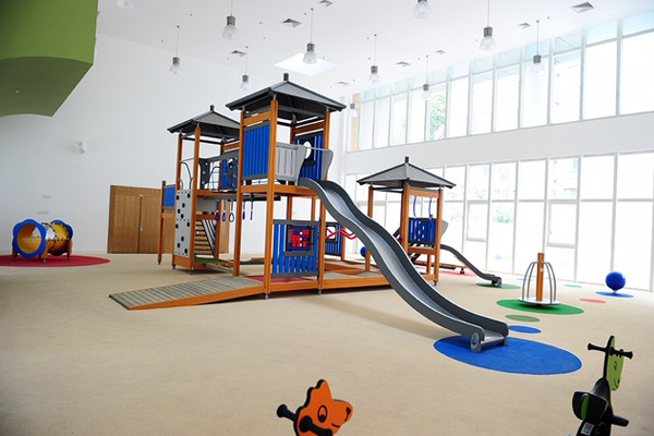 Indoor playground flooring with custom hand cut colored circled flooring that complies with playground fall height requirements. There are a few different play structures including two slides and a tunnel.