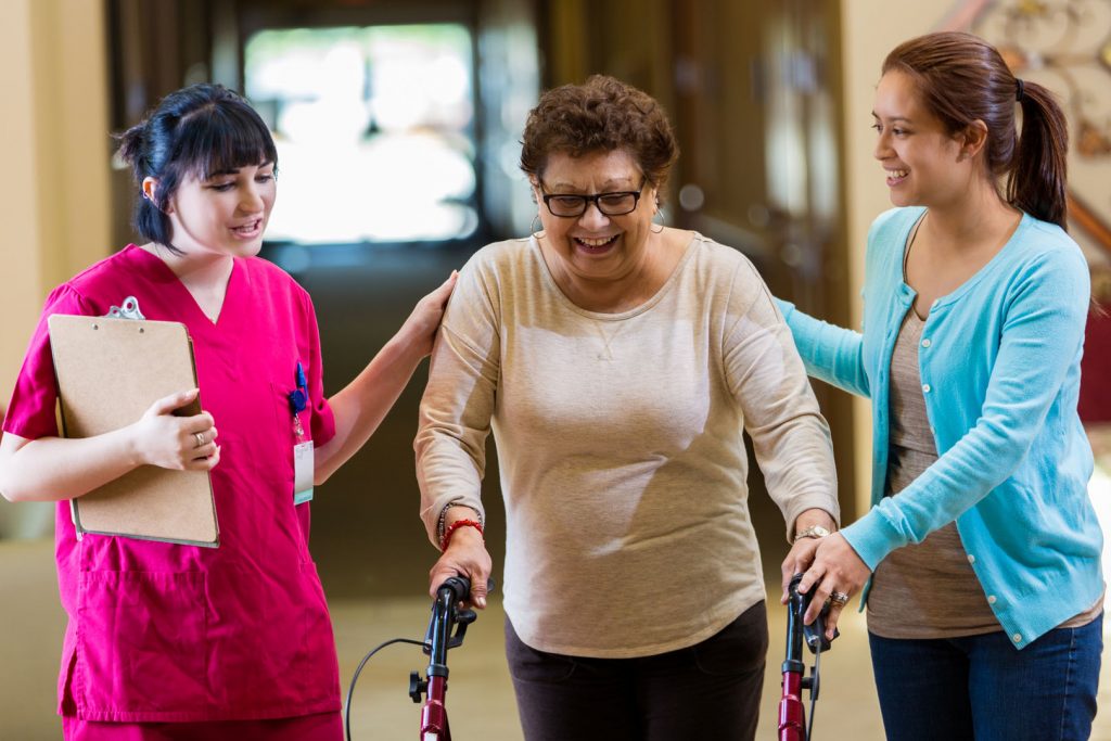 An elderly lady using a walker being assisted by two woman in a physical therapy center.