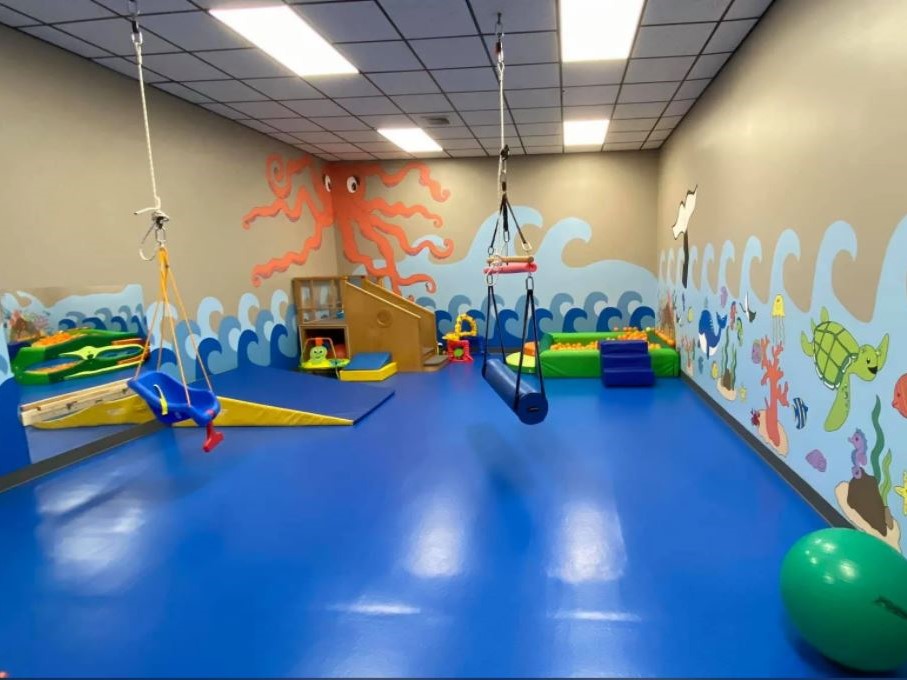 Blue impact attenuating flooring in pediatric therapy center. The walls are painted with ocean animals and waves.